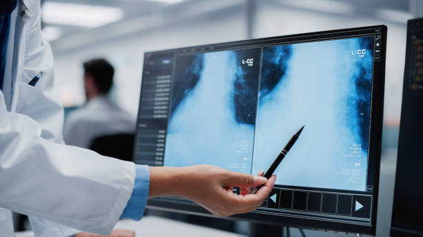 istock Medical Hospital: Two Doctors Talk and Use Computer, Point at Screen, Analysing Patient X-ray, Doing Test Results Analysis. Health Care Clinic Laboratory: Surgeon and Physician Finding Treatment 1388387892