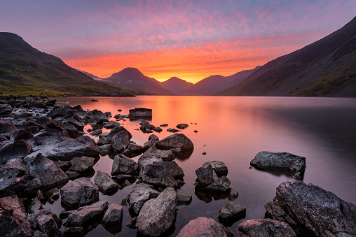 Colourful Orange And Red Sky At Sunrise With Rocks On The Lake Shoreline. Lake District, UK.