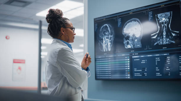 의학 병원: 자신감 흑인 여성 신경학자, 신경 과학자, 신경 외과 의사, 뇌 이미지와 mri 스캔으로 tv 화면을 보고, 아픈 환자 치료 방법에 대해 생각. 생명을 구하는 것 - 의료 연구 뉴스 사진 이미지