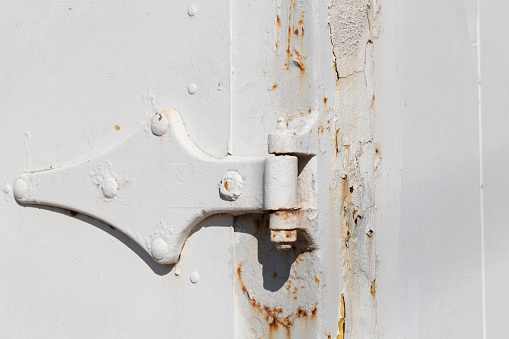 Rusty hinge of old weathered industrial cargo shipping container on a sunny day in springtime.