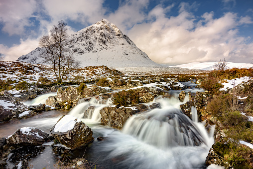 The iconic viewpoint featuring a stunning waterfall with Buachaille Etive Mor in the background, covered in a fresh layer of snow. Glencoe, Scottish Highlands, UK.