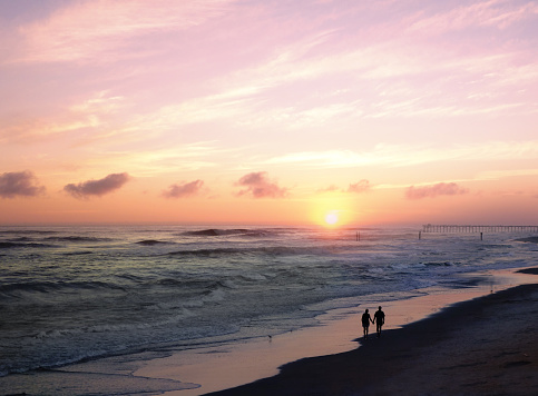 A couple holding hands walking along the beach at sunset in Carolina Beach North Carolina