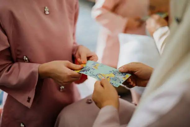Malay Muslim parents in traditional clothings giving gift of money to their children during Hari Raya Aidilfitri celebration