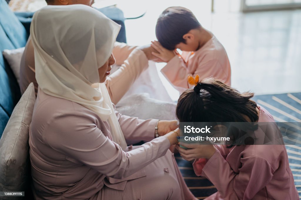 Malay Muslim children in traditional clothings asking forgiveness to their parents during Hari Raya Aidilfitri celebration Bowing Stock Photo