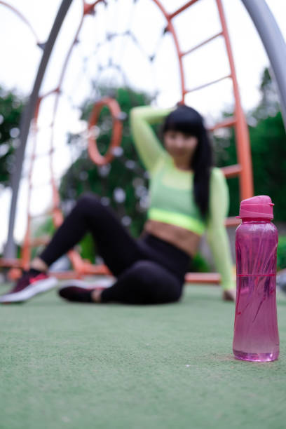 charmante fitness sport girl in mode schwarz und grün sportswear mit einer rosa flasche wasser auf sportlich trendigem spielplatz auf der straße - exercising sensuality water bottle relaxation exercise stock-fotos und bilder