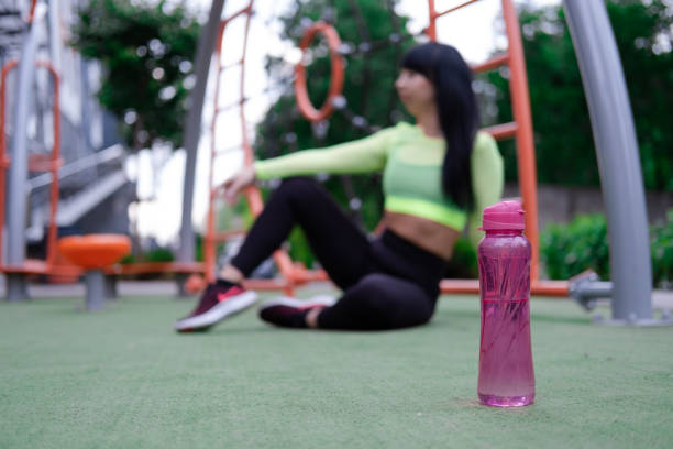 charmante fitness sport girl in mode schwarz und grün sportswear mit einer rosa flasche wasser auf sportlich trendigem spielplatz auf der straße - exercising sensuality water bottle relaxation exercise stock-fotos und bilder