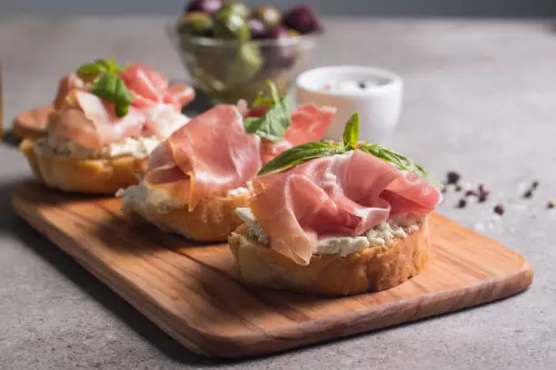 Bruschetta with prosciutto, basil, olives, spices and herbs. Appetizers.