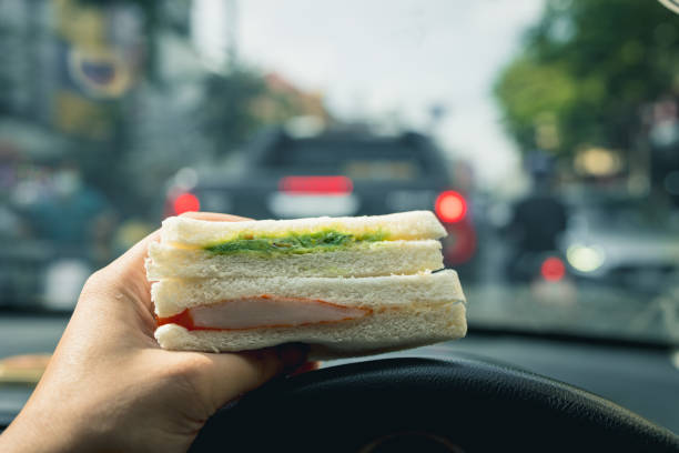 Male hand holding a sandwich in the car, morning rush hour in the city stock photo