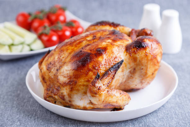 pollo cotto intero in una deliziosa crosta. un piatto tradizionale. sullo sfondo ci sono cetrioli e pomodorini su un piatto bianco. grande pla - rotisserie roast chicken chicken roasted foto e immagini stock