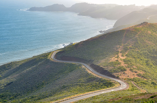 Winding road along the coast of California with fog rolling in from the ocean at sunset