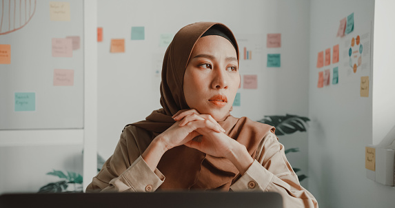 Frustrated young muslim businesswoman wearing hijab working on a laptop sitting at desk in office.