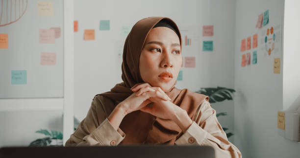 Frustrated young Asian muslim businesswoman wearing hijab working on a laptop sitting at desk in office. Frustrated young muslim businesswoman wearing hijab working on a laptop sitting at desk in office. meditation room office stock pictures, royalty-free photos & images