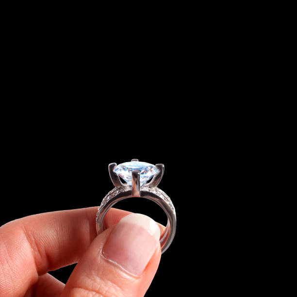 feche os dedos femininos segurando anel de diamante sobre fundo preto - wedding bride buying caucasian - fotografias e filmes do acervo