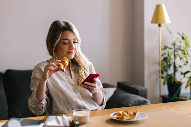 istock Woman Eating Croissant While Using Her Cell Phone 1388404018