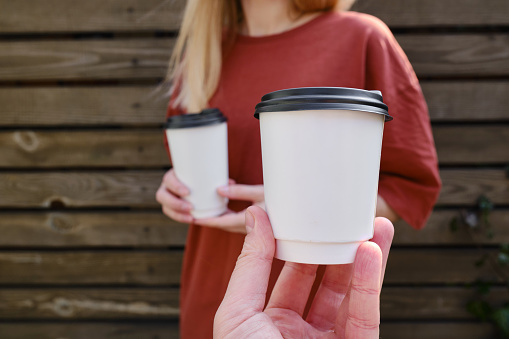 White paper cup with coffee in the hand of a woman and a man. Time to drink coffee in the city. Coffee to go. Enjoy the moment, take a break. Disposable paper cup close-up. Delicious hot drink. Mockup