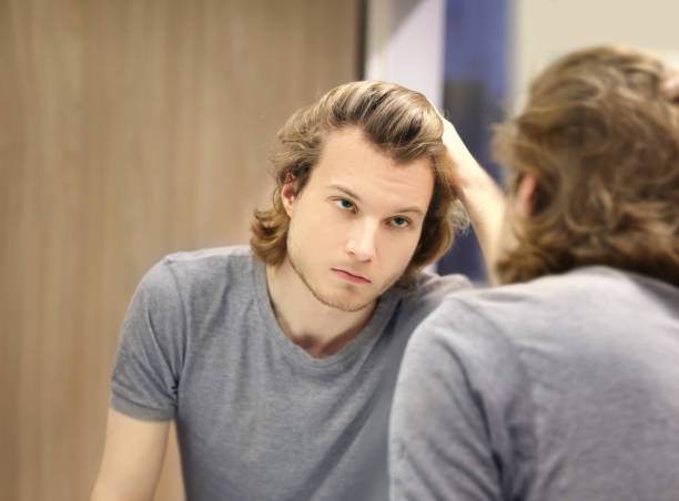 istock young man looking in the mirror,combing his hair,looking at problems on face 1388406376