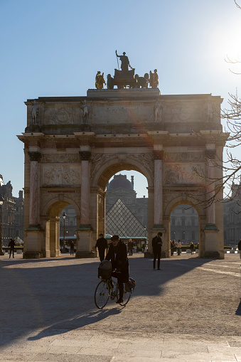 The Arc de Triomphe de Carrousel in Paris France, in the foreground are tourists walking from the Louvre museum.