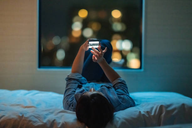 Woman lying down on bed and using smart phone at night stock photo