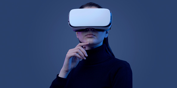 Young beautiful woman wearing a VR headset and experiencing virtual reality, futuristic technology concept