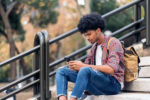 Stock photo of handsome young african guy sitting in stairs and using his phone.