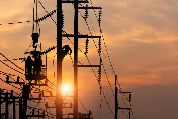 istock Silhouette electrician on electric power pole with blurred sunset sky background, silhouetted electrician team working on poles to install high-voltage equipment 1388412019