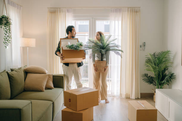 Happy couple moving new house. Happy man and woman carrying boxes together into their new home. looking around stock pictures, royalty-free photos & images