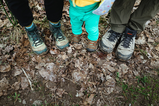 A young Caucasian family of three on a hike in the woods.  Detail shot of their boots: father, mother, and toddler.