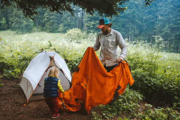 Father and daughter are setting up camping tent family vacations travel lifestyle hiking outdoor in forest adventure weekend trip stock photo