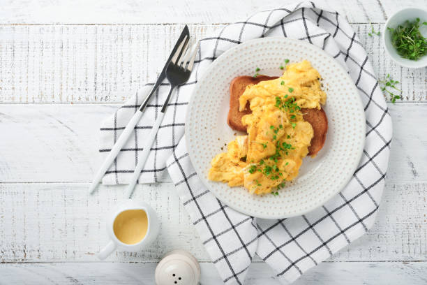 istock Scrambled Eggs. Fluffy and Buttery scrambled eggs on bread with microgreen radish and hollandaise sauce on white plate over white wooden background. Homemade breakfast or brunch meal. Top view. 1388418695