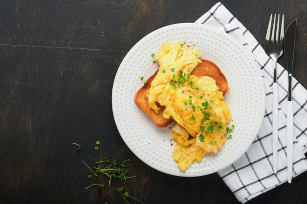 istock Scrambled Eggs. Fluffy and Buttery scrambled eggs on bread with microgreen radish and hollandaise sauce on white plate over dark old wooden background. Homemade breakfast or brunch meal. Top view. 1388418759