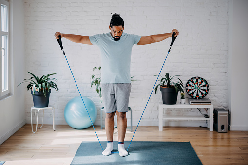 Full length profile shot of a guy exercising with a stretching band at home