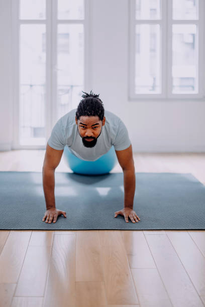 istock Handsome black man doing exercise and stretching , practicing flexibility with pilates ball at the home. 1388419278
