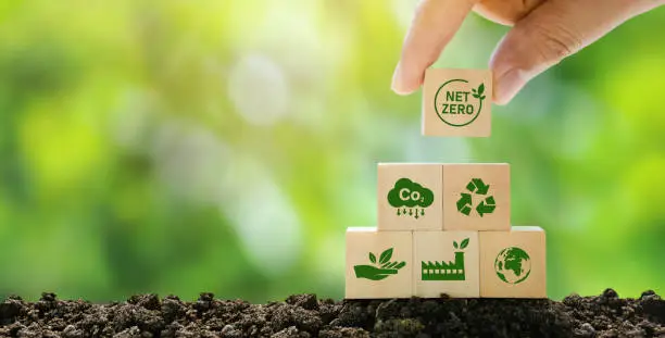 Photo of Net Zero and Carbon Neutral Concepts Net Zero Emissions Goals A climate-neutral long-term strategy Ready to put wooden blocks by hand with green net center icon and green icon on gray background.