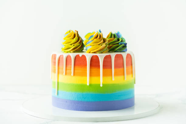 istock Rainbow cake with whipped cream top on the white background. Birthday cake with multicolored cream cheese frosting 1388422206