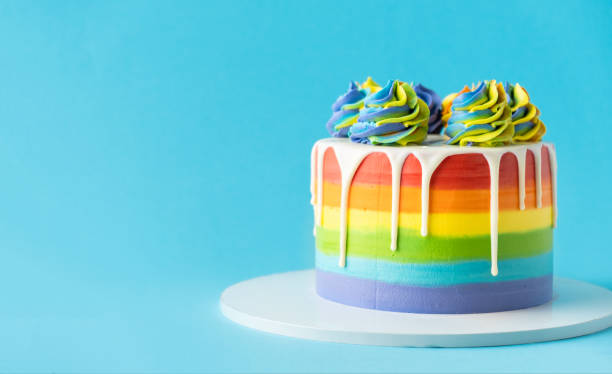 istock Rainbow cake with whipped cream top on the blue background. Birthday cake with multicolored cream cheese frosting 1388422208