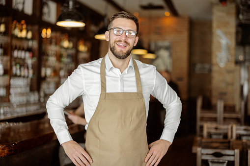 Portrait of bearded happy barista standing at a trendy coffee shop, cafe - small business concept