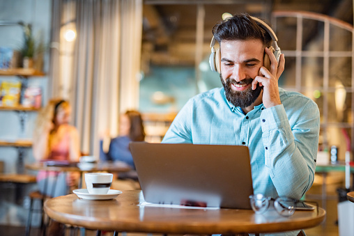 Young male student looking at laptop and using headphones in coffee shop