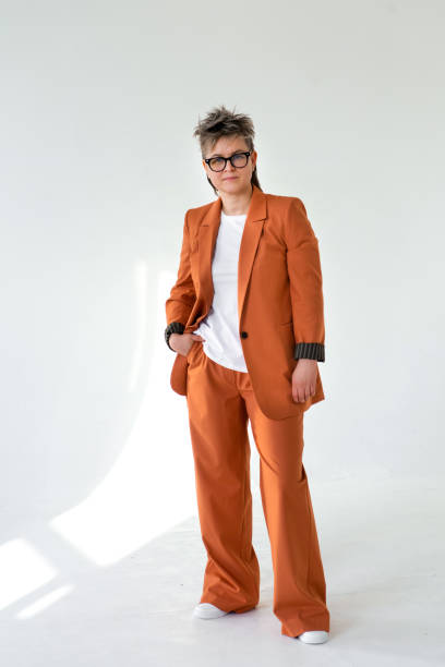 young emotional non binary person wearing orange color suit posing at studio