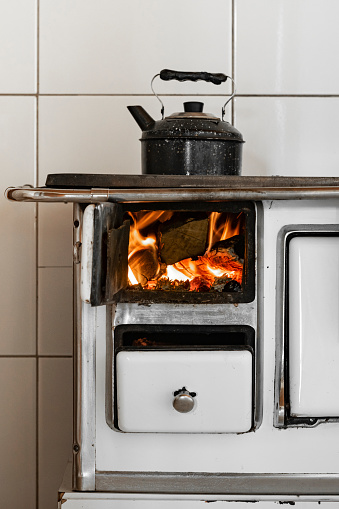 Image with fire flames inside a white wood burning stove and a black kettle