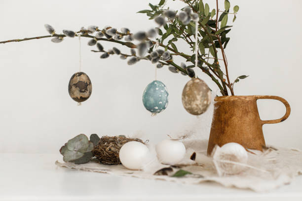 Easter rustic still life. Natural dyed easter eggs, willow branches in vase, feathers, nest on linen napkin on aged wooden table. Happy Easter! Simple stylish easter decoration on table aesthetics bodegón rústico de semana santa. huevos de pascua teñidos naturales, ramas de sauce en jarrón, plumas, nido en servilleta de lino sobre mesa de madera envejecida. ¡felices pascuas! decoración de pascua sencilla y elegante en la estética de la mesa