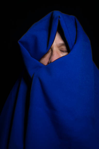 istock Man covered with blue cloth against a black background. 1388430338