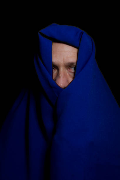 istock Man covered with blue cloth against a black background. 1388430339