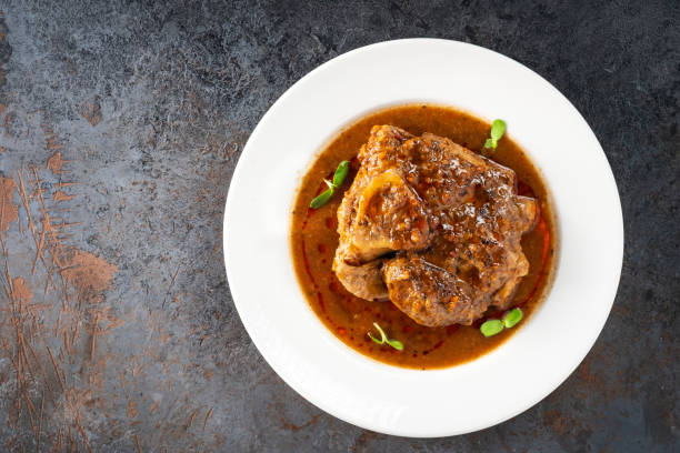 Stewed Osso Buco dish with tomato gravy on a white plate and a stone background, top view Stewed Osso Buco dish with tomato gravy on a white plate and a stone background, top view ossobuco stock pictures, royalty-free photos & images