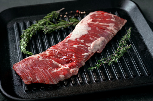 Raw machete steak on beef in a grill pan with seasoning. Stone background.