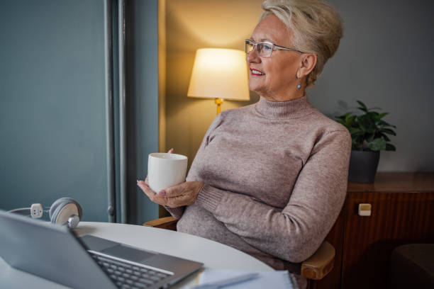 istock Senior woman drinking coffee and using laptop at home 1388432563