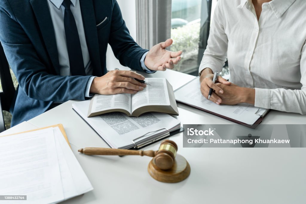 Male lawyer is pointing on legal document to explaining about consultation terms and condition to businesswoman before signing on contract at law firm Male lawyer is pointing on legal document to explaining about consultation terms and condition to businesswoman before signing on contract at law firm. Law Stock Photo