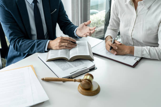 Male lawyer is pointing on legal document to explaining about consultation terms and condition to businesswoman before signing on contract at law firm stock photo