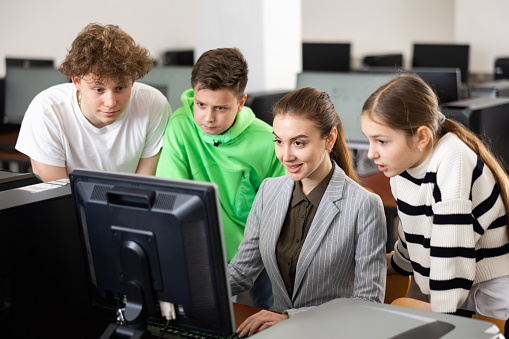 Modern interested teen schoolchildren learning basics of programming with friendly female teacher in computer college