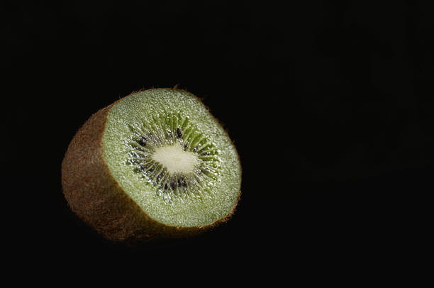 Half of a single kiwi fruit on a black background.
