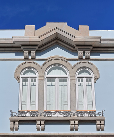 Tripartite window with iron guard and decorated pilasters on the second story of the west-pale blue painted façade of a Revivalist style mansion in Old Town-Vila Adentro area. Faro-Algarve-Portugal.